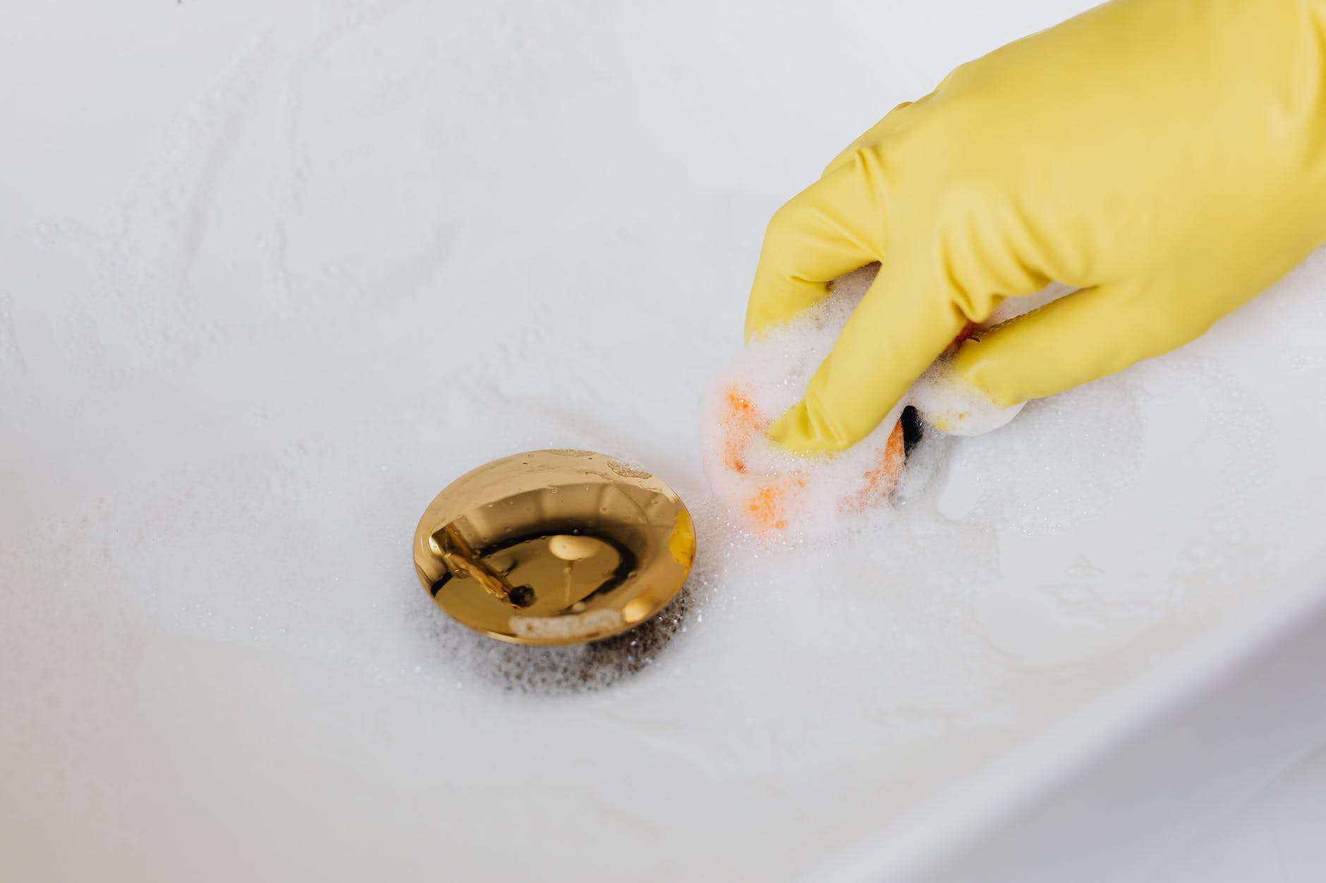 person in glove using sponge and detergent for washing bathroom sink