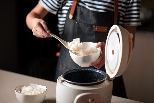 Crop person taking out boiled rice from a rice cooker